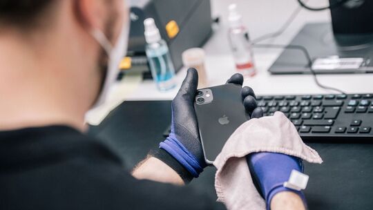 Ein Mitarbeiter überprüft ein refurbished Iphone Ein Mitarbeiter überprüft ein refurbished Iphone