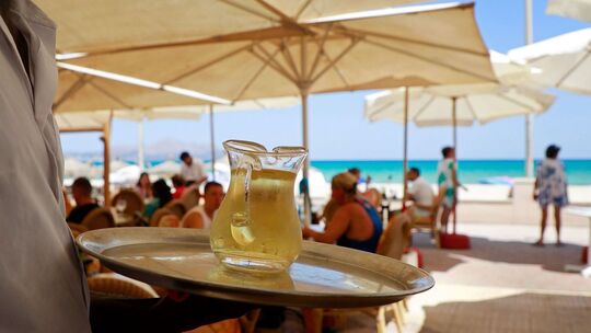 Ein Kellner serviert an einem mallorquinischen Strand einen Wein Ein Kellner serviert an einem mallorquinischen Strand einen Wein