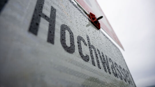 Regentropfen hängen an einem Schild, das vor Hochwasser warnt, Wolken am Himmel verheißen weiteren Niederschlag. Zum Ende der Pf Regentropfen hängen an einem Schild, das vor Hochwasser warnt, Wolken am Himmel verheißen weiteren Niederschlag. Zum Ende der Pf