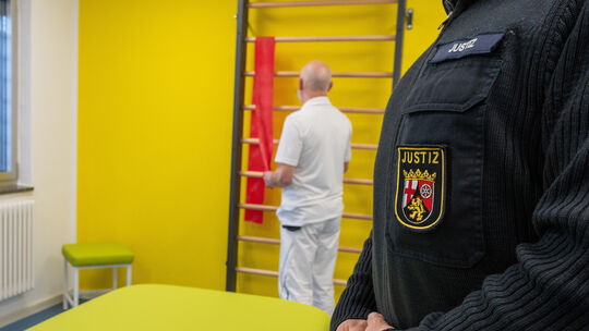 Ein Justizbeamter der Justizvollzugsanstalt (JVA) Wittlich steht im Raum für Physiotherapie, während ein Therapeut Vorbereitunge Ein Justizbeamter der Justizvollzugsanstalt (JVA) Wittlich steht im Raum für Physiotherapie, während ein Therapeut Vorbereitunge