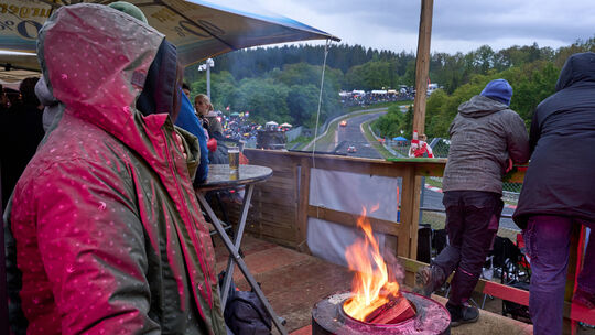Zuschauer des 24-Stunden-Rennens auf dem Nürburgring wärmen sich bei kaltem Wetter an einem Feuer. Zuschauer des 24-Stunden-Rennens auf dem Nürburgring wärmen sich bei kaltem Wetter an einem Feuer.