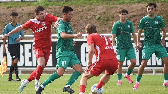 Umzingelt: Der Baumholderer Kapitän Marius Gedratis (grünes Trikot) muss sich in Hüffelsheim spielerisch befreien. Die Szene beo Umzingelt: Der Baumholderer Kapitän Marius Gedratis (grünes Trikot) muss sich in Hüffelsheim spielerisch befreien. Die Szene beo